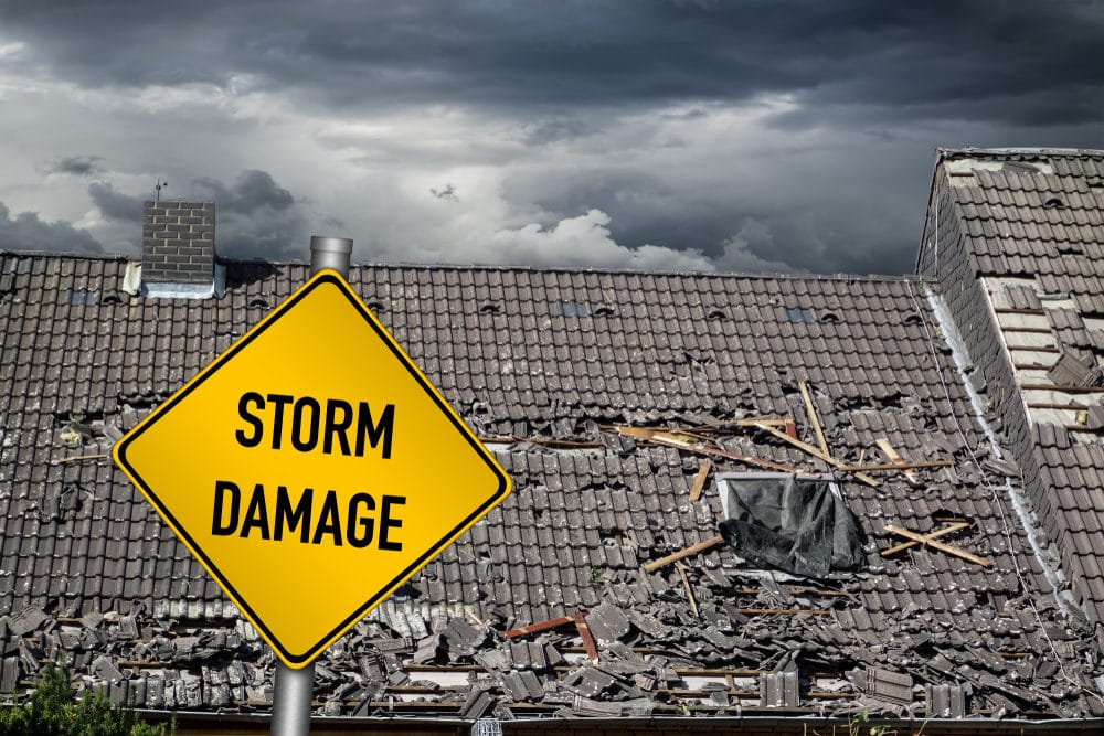 Yellow damage warning sign in front of roof of house damaged by heavy hurricane tornado storm.