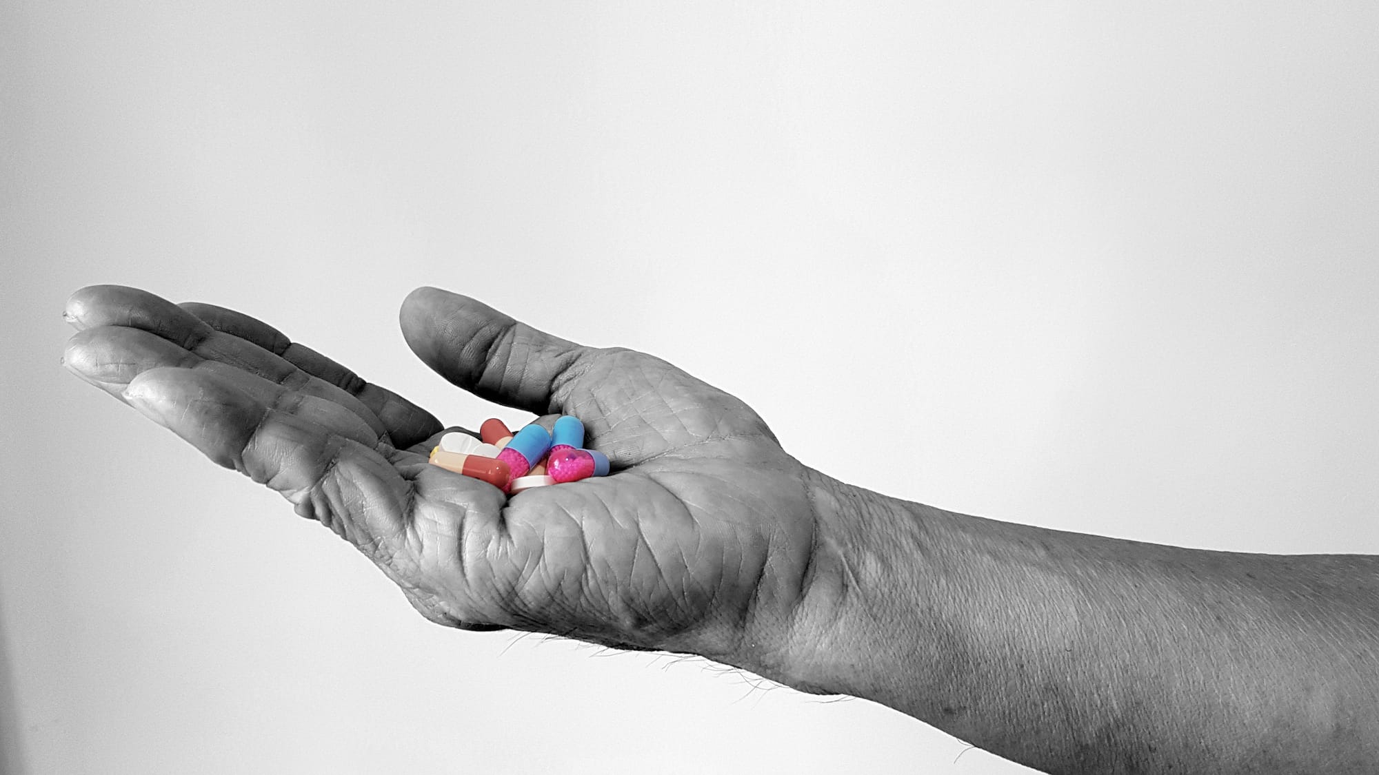 Black and white image of a man's hand holding a variety of multi-colored pills.