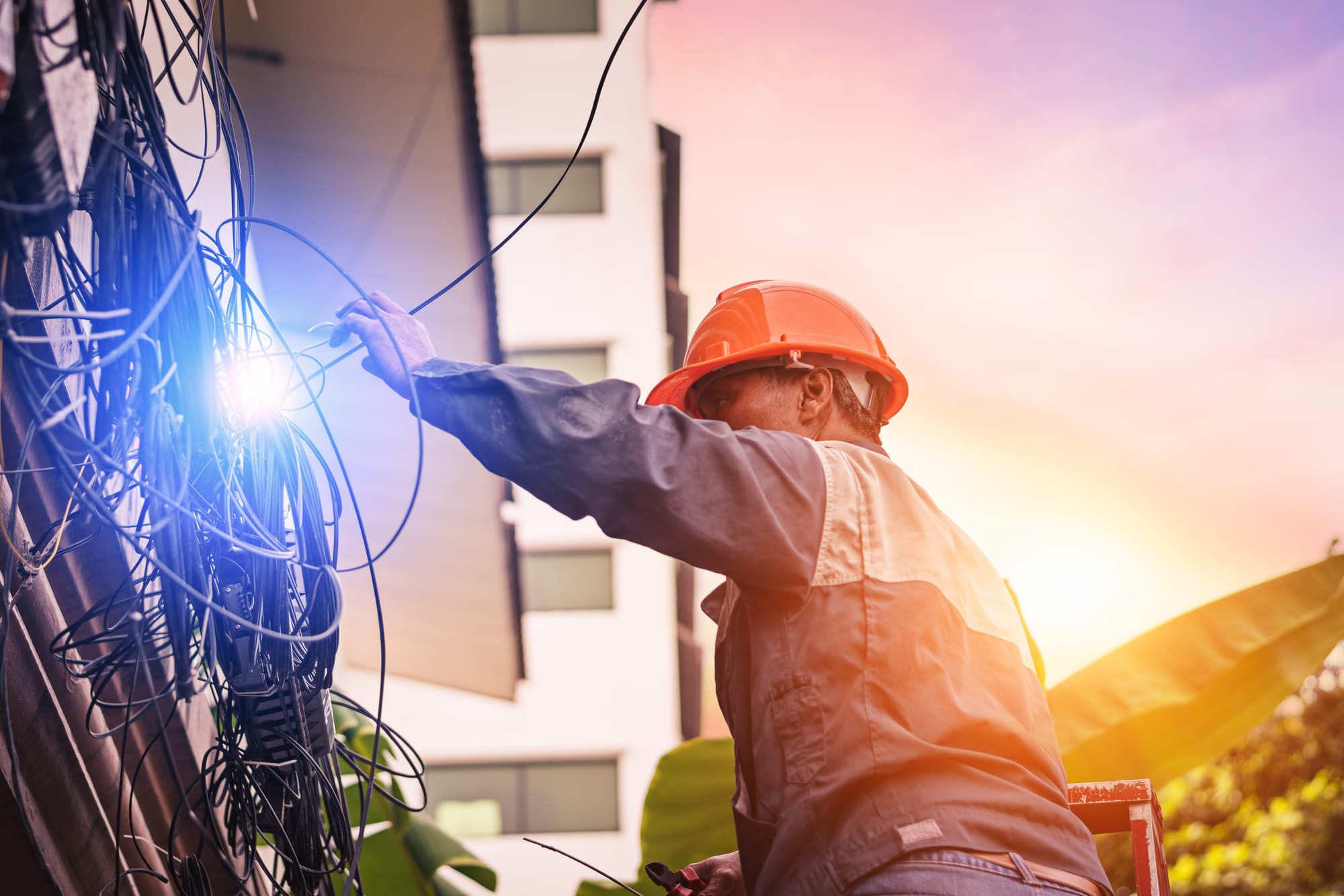 Electrical worker on a ladder fixing electrical lines with the sun setting.