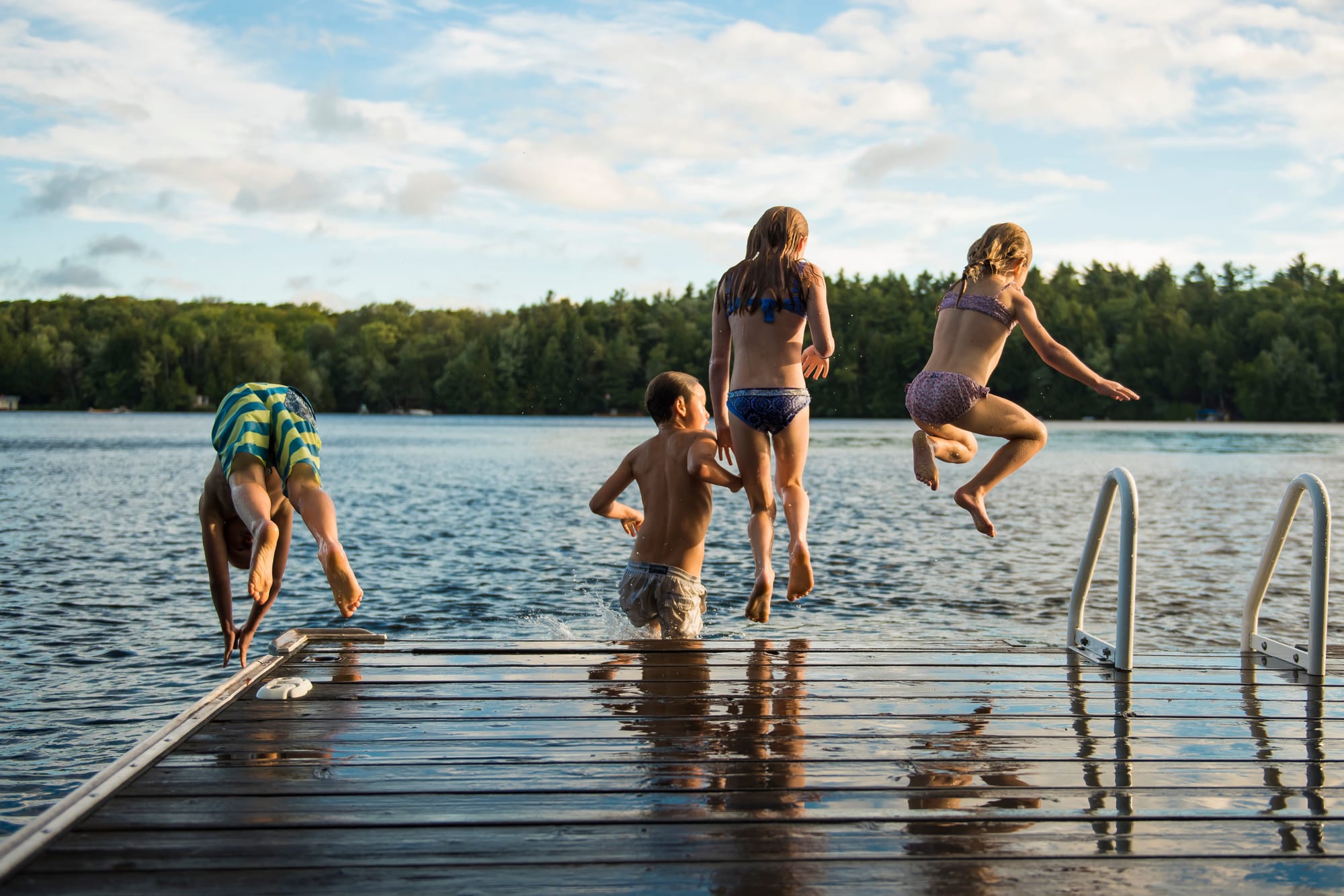 View from behind a group of kids jumping into a lake from a dock.