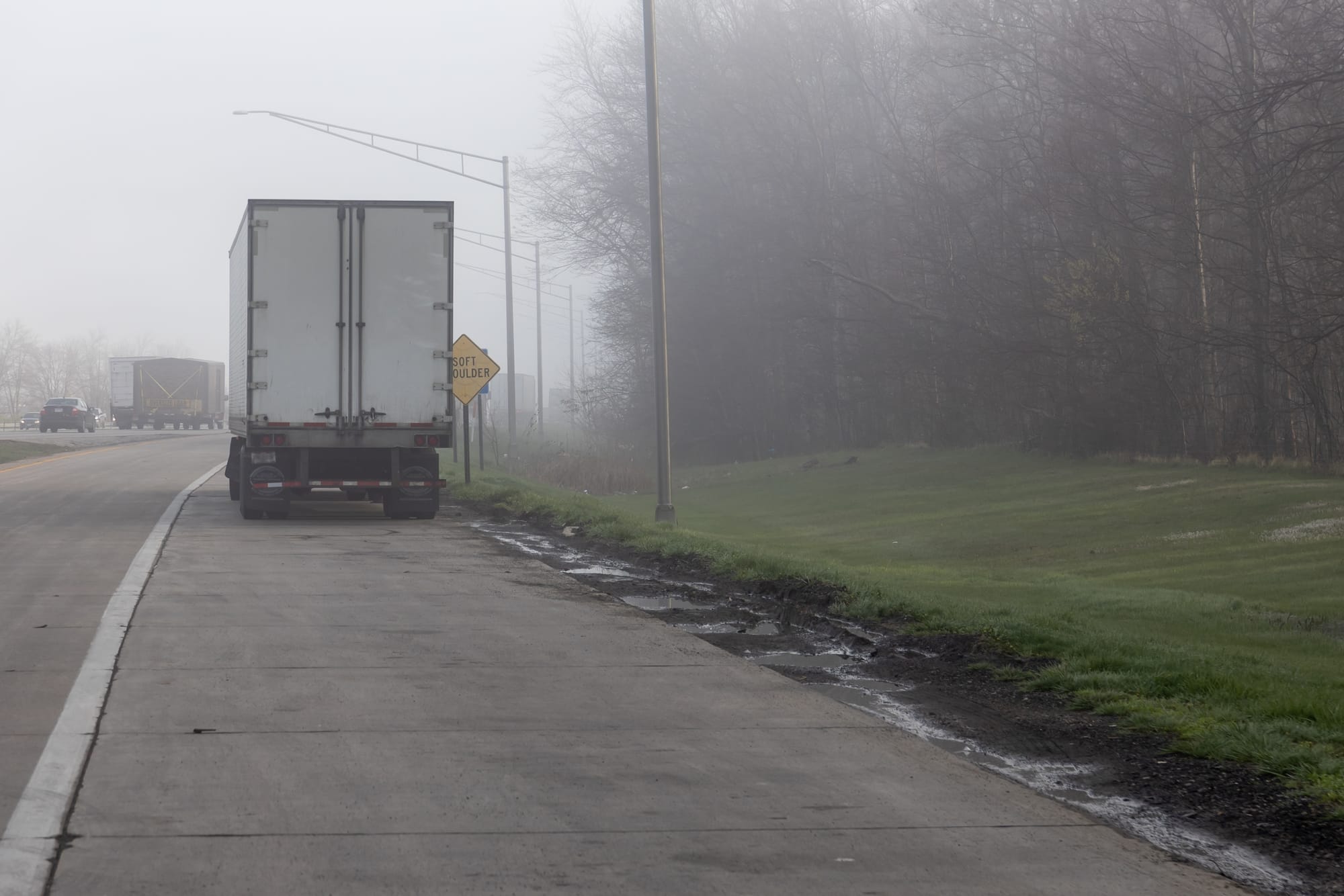 A white semi-truck parked on the side of a highway in foggy weather.