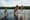 View from behind a group of kids jumping into a lake from a dock.