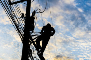 Silhouetted electricians working at electric pole in blue sky